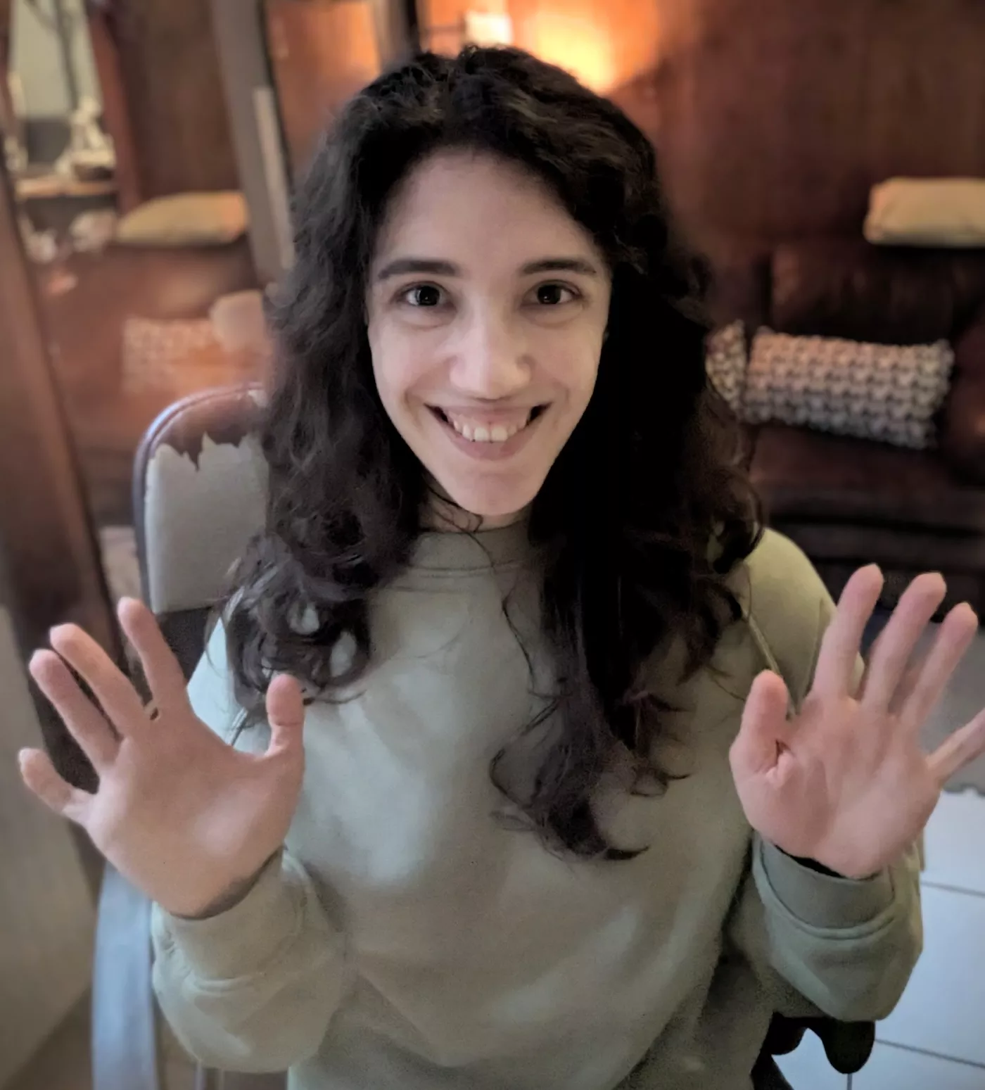 young person with beaming smile and long dark hair waving at the camera with both hands